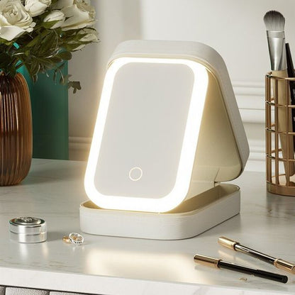 Lighted makeup mirror on a desk with beauty products and flowers in the background